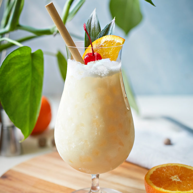 painkiller cocktail in a hurricane glass with orange and cherry garnish