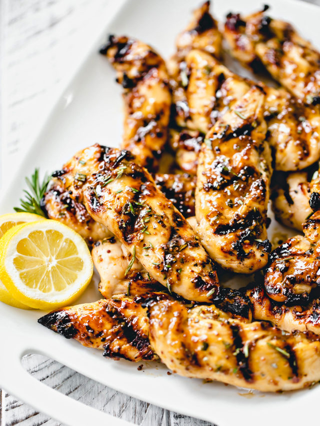 white platter with grilled honey mustard chicken next to fresh rosemary and lemon slices