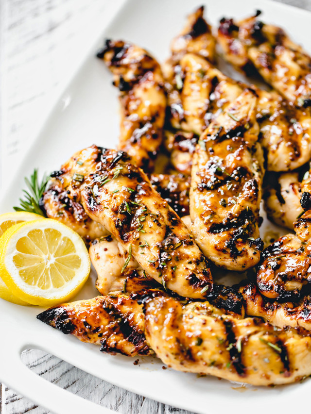 white platter with grilled honey mustard chicken next to fresh rosemary and lemon slices