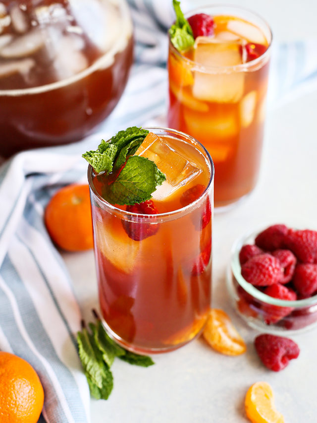 photo of two glasses of raspberry iced tea with a kitchen towel and bowl of raspberries