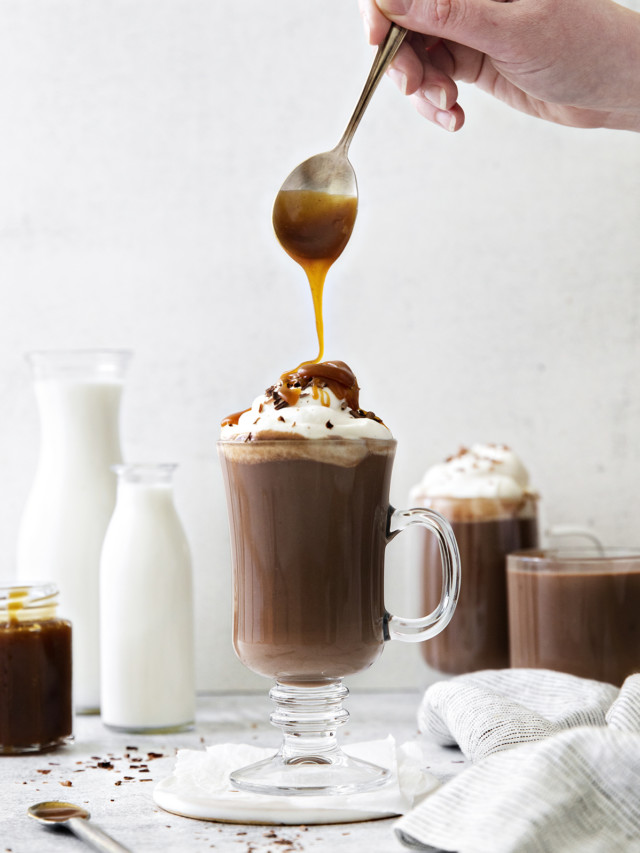 photo of salted caramel hot chocolate in a clear mug with caramel being drizzled on the top