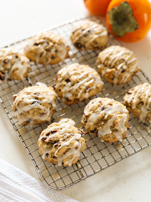 persimmon cookies drizzled with orange glaze on a wire rack with fresh persimmon in the background