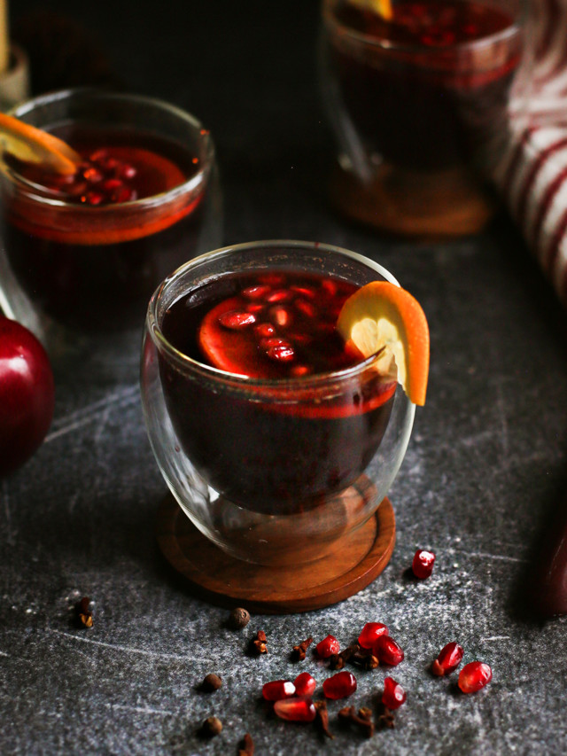 photo of glasses of spiced apple cider on a dark table with a candle