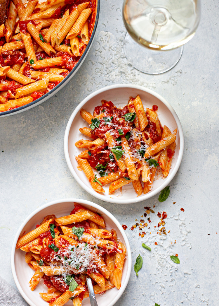 two plates of penne arrabbiata and a glass of wine