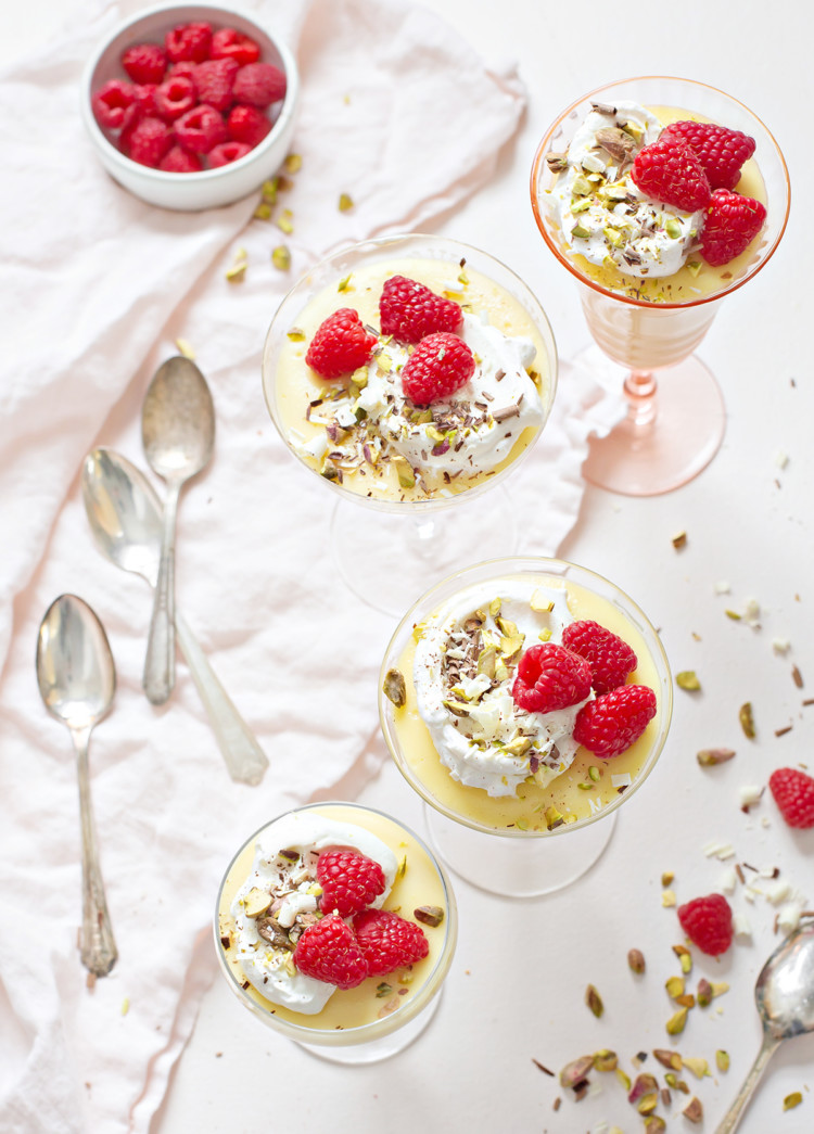 dishes of white chocolate pudding garnished with whipped cream and raspberries arranged