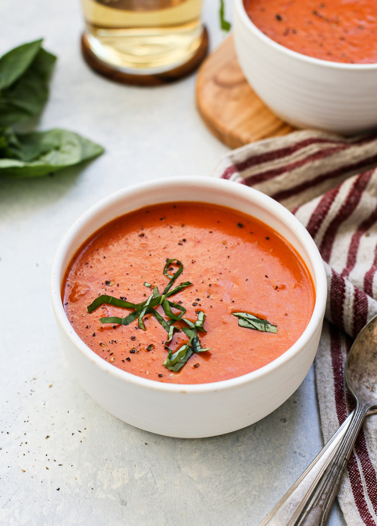 photo of a white bowl of cream of tomato soup on a light blue background