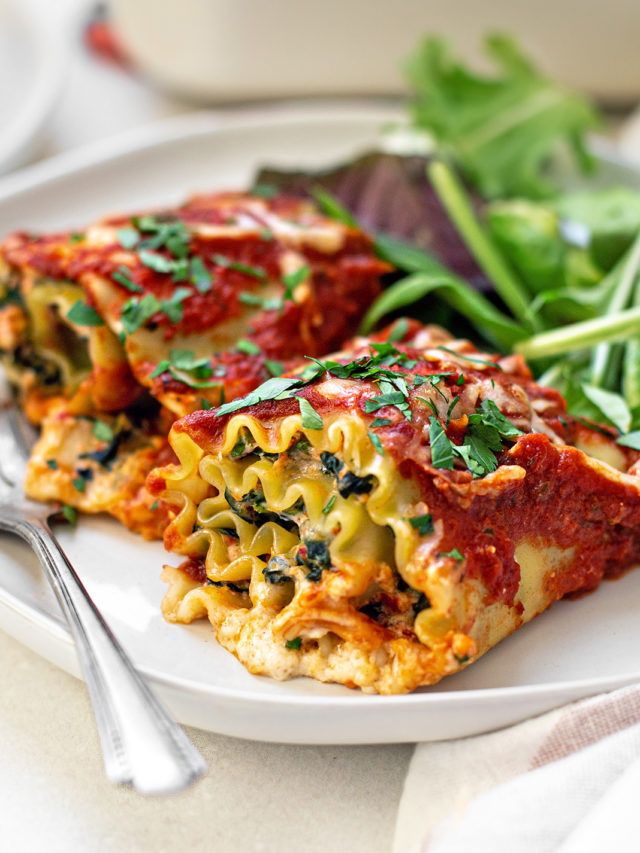 two spinach lasagna rolls on a white plate with a fork and green salad