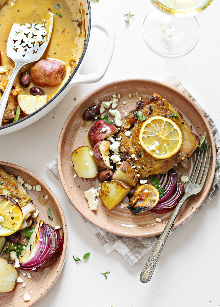 overhead photo of greek chicken thighs on a plate with potatoes, lemons, olives, and feta