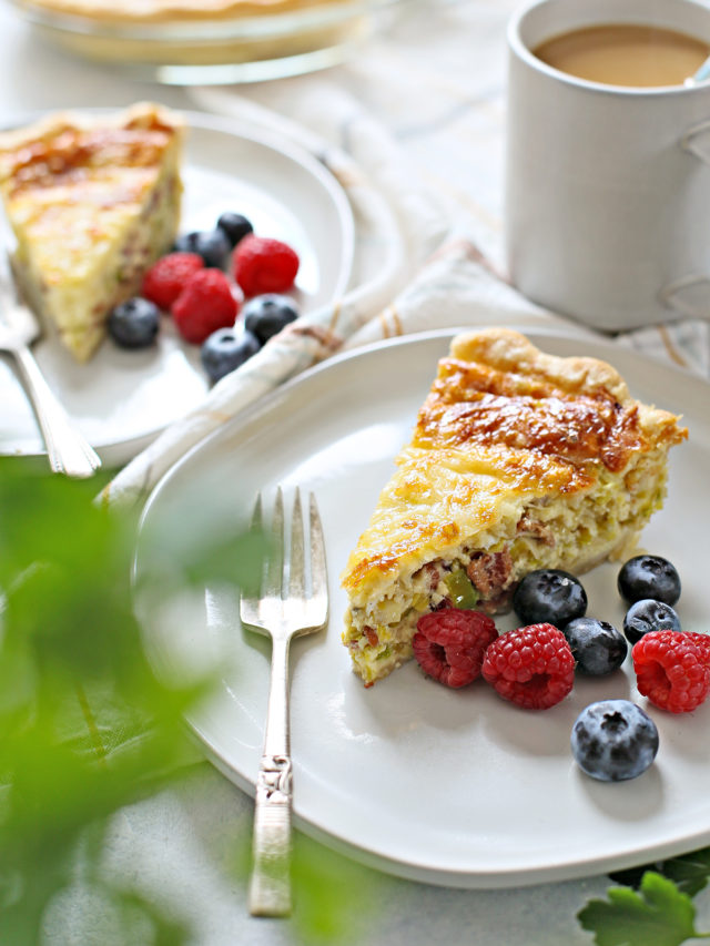 a table set with two plates of quiche lorraine, fresh berries, and a cup of coffee