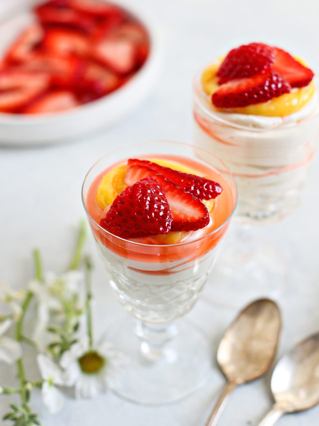 two spoons with two dessert dishes of cheesecake mousse topped with lemon curd and fresh strawberries