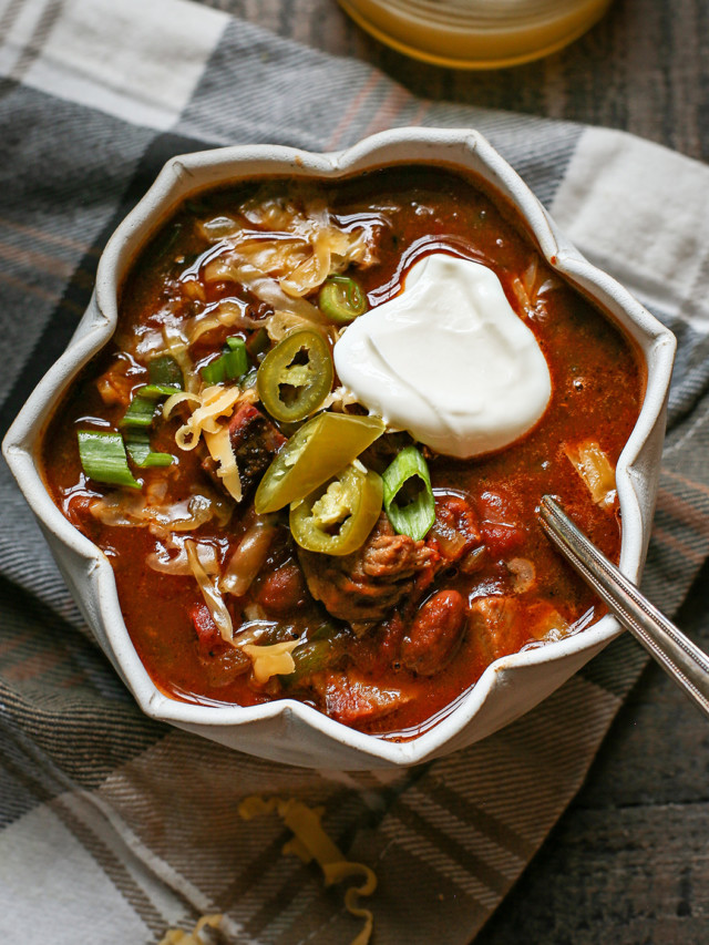 a bowl of brisket chili topped with sour cream, jalapeno, and green onion