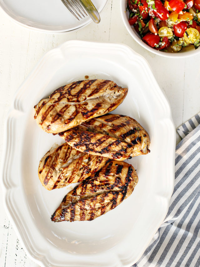 a white platter with cooked grilled chicken breasts that were marinated using balsamic chicken marinade