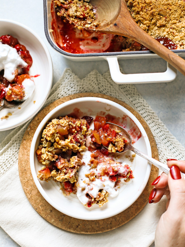 woman eating apple cranberry crisp from a white bowl