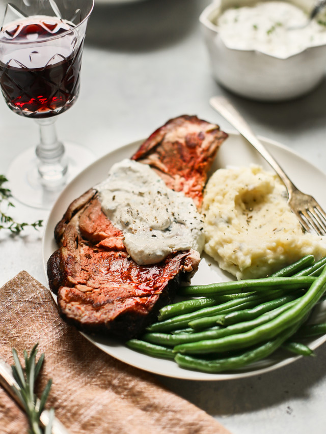 a slice of smoked prime rib on a plate with green beans and mashed potatoes