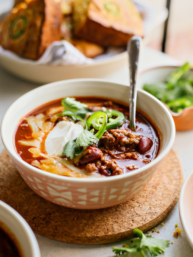 bowl of ground beef chili topped with sour cream, jalapeno, cheese, and cilantro