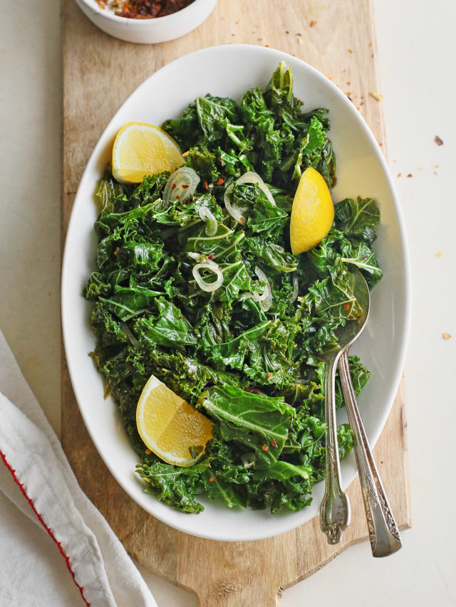 a white bowl of garlic sauteed kale on a wooden cutting board