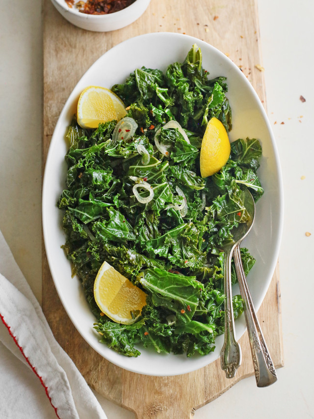 a white bowl of garlic sauteed kale on a wooden cutting board