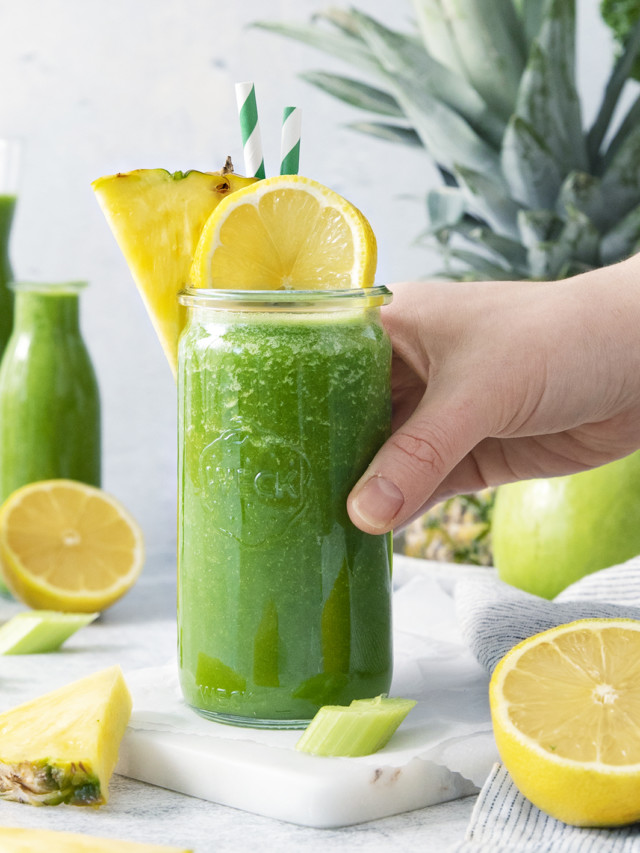 woman picking up a glass of pineapple kale smoothie