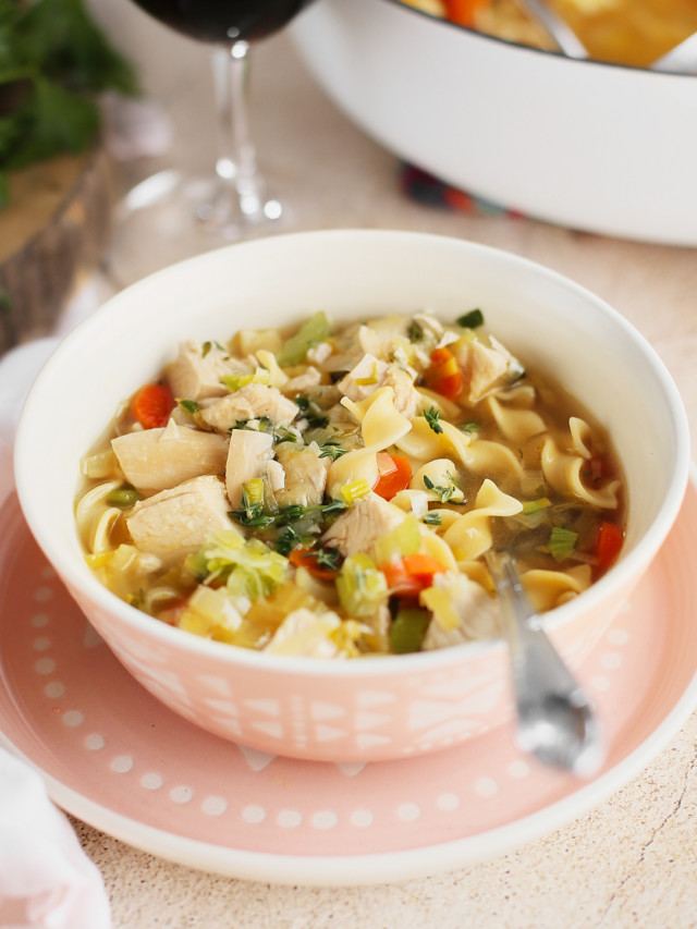 bowl of homemade chicken noodle soup from scratch next to a glass of wine