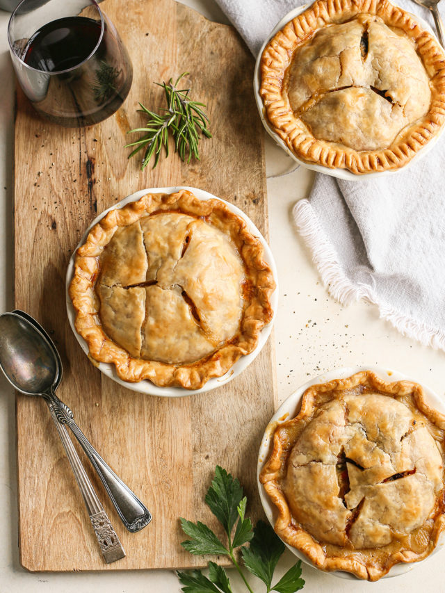 3 mini chicken pot pies on a wooden cutting board with a glass of red wine