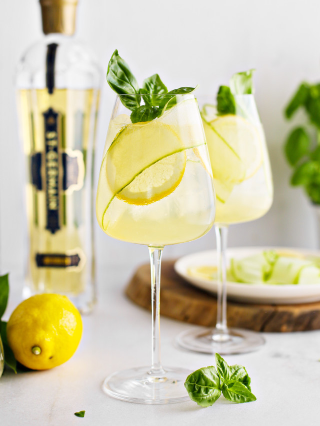 two glasses of st germain spritz garnished with lemon slices, cucumber ribbon, and fresh basil