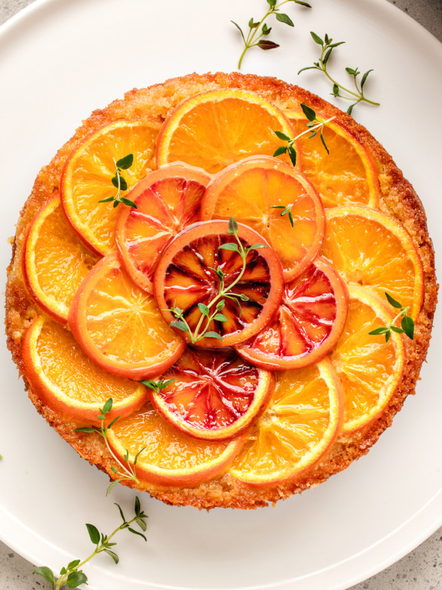 orange upside down cake on a white plate decorated with fresh thyme