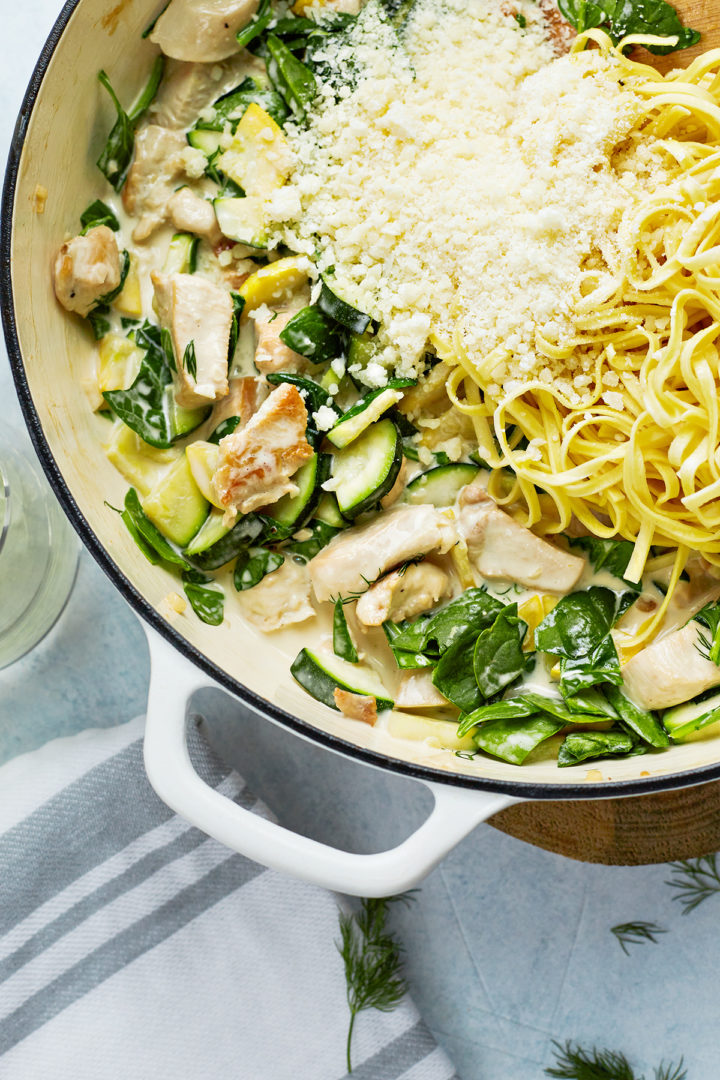 adding the parmesan cheese and the noodles to the creamy pasta primavera