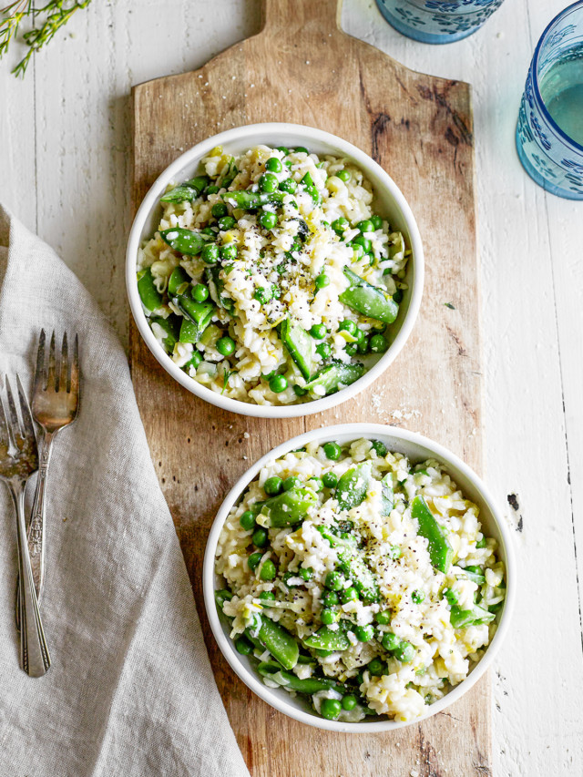 pea risotto served in two white bowls on a wooden board