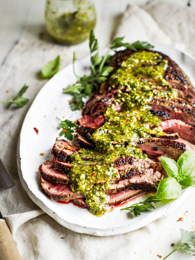 sliced chimichurri skirt steak on a white platter with chimichurri sauce