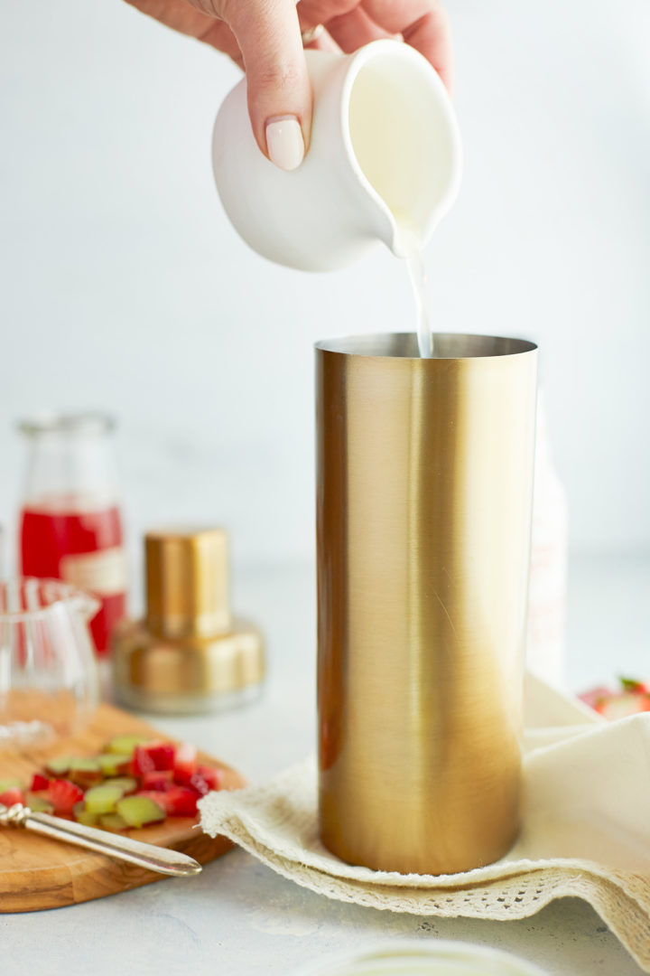 woman adding lemon juice to the cocktail shaker to make a strawberry whiskey sour