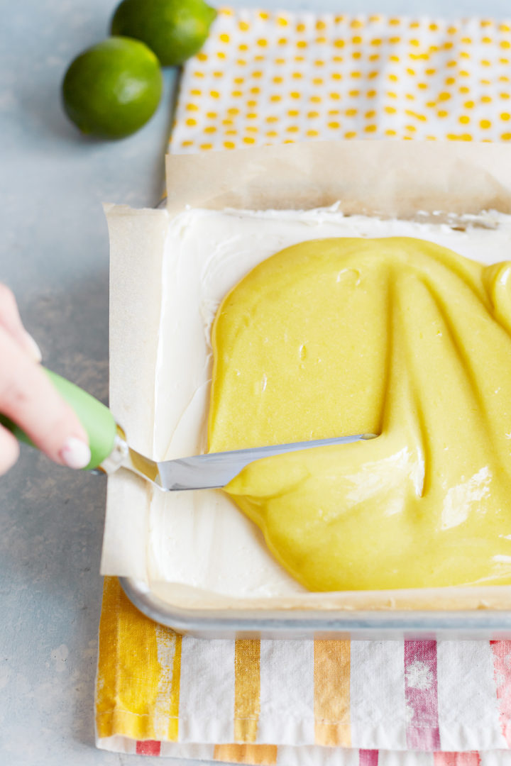 woman spreading lime curd on top of the cheesecake bars