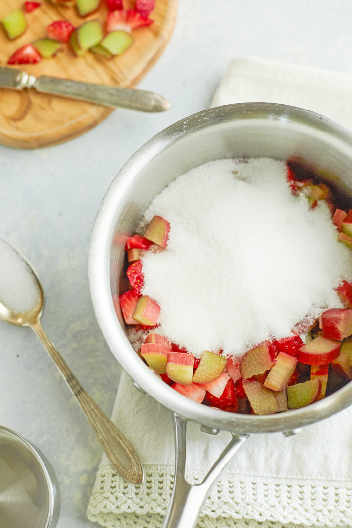 making ingredients (sugar, strawberries, rhubarb, water) in a stainless steel pot to make the simple syrup for this strawberry rhubarb cocktail