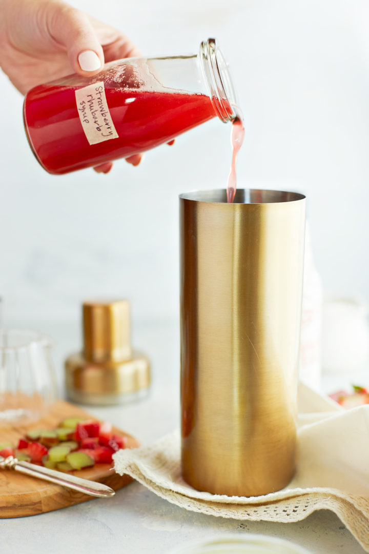 woman adding strawberry rhubarb simple syrup to the other ingredients in this strawberry rhubarb cocktail 