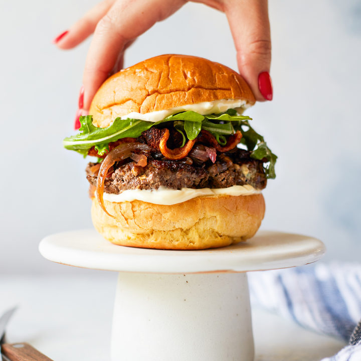 woman placing a bun on a blue cheese burger