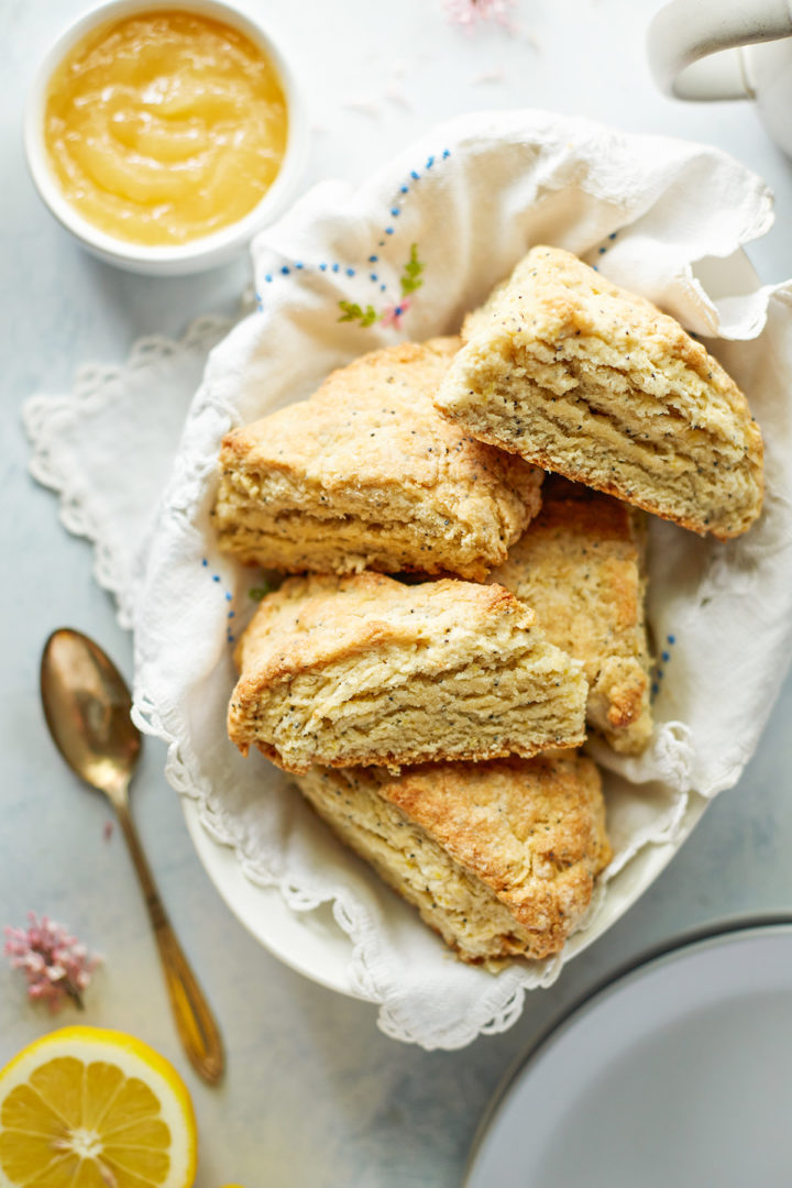 a basket of lemon poppyseed scones next to a bowl of lemon curd