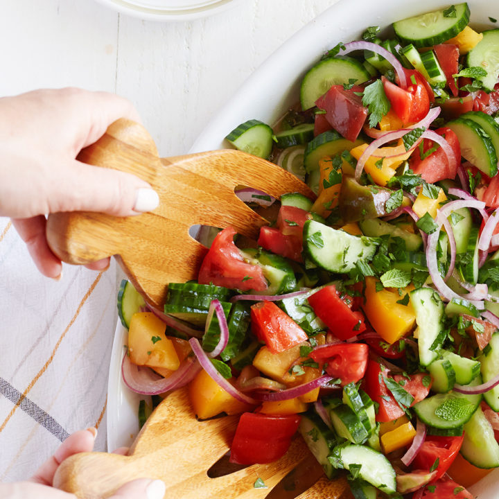 woman serving a cucumber tomato onion salad