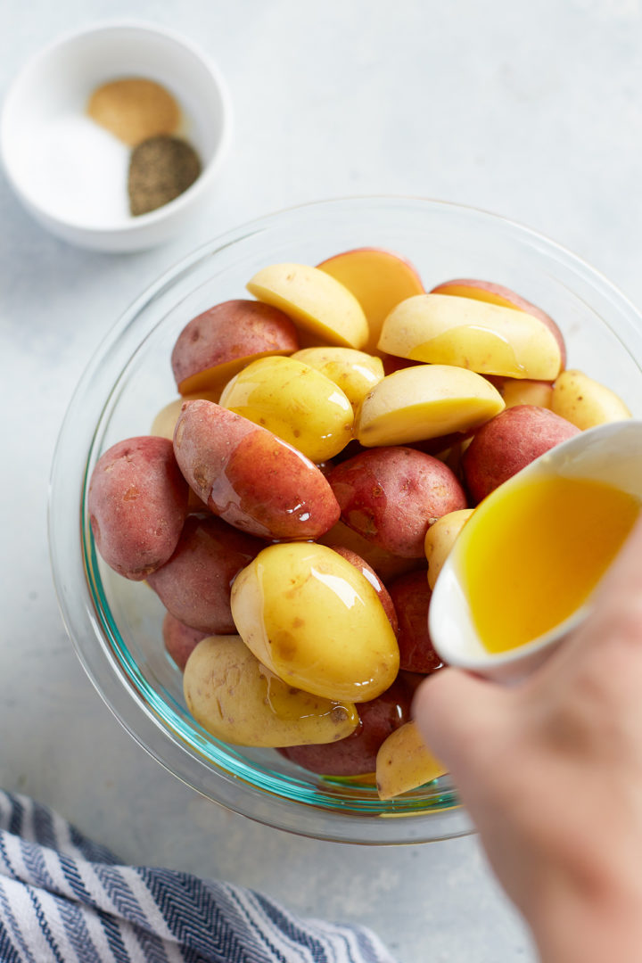 woman pouring melted ghee over a bowl of baby potatoes