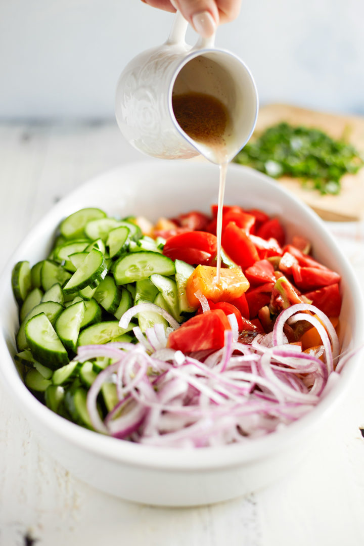 woman adding vinegar dressing to cucumber tomato and onion salad