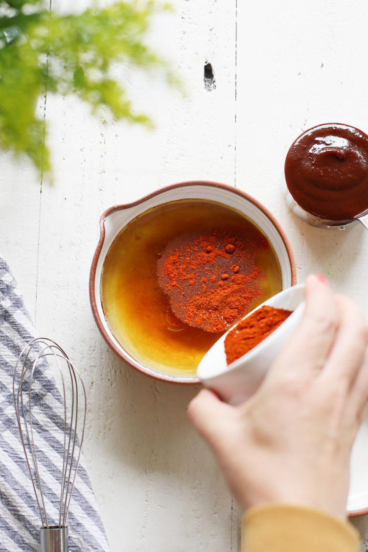 woman adding spices to a bowl of bbq chicken marinade