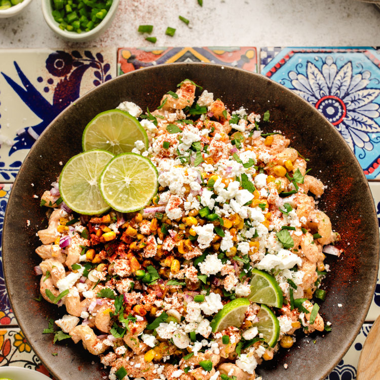 overhead photo of a bowl of Mexican street corn pasta salad garnished with lime slices