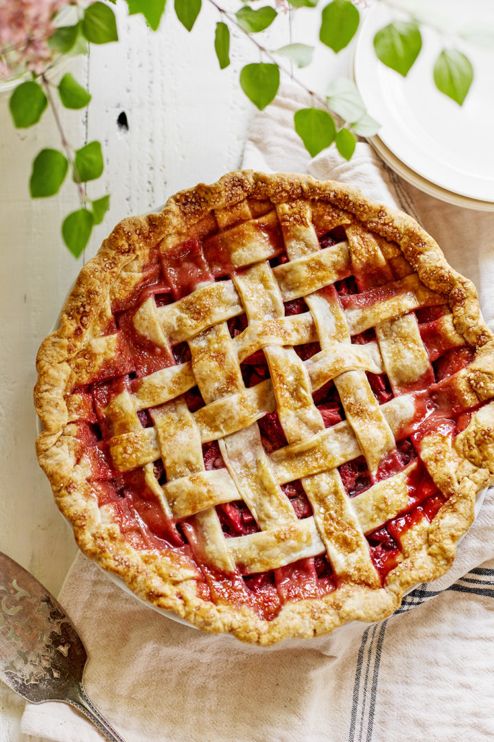 strawberry and rhubarb pie with a lattice crust on a white wooden table