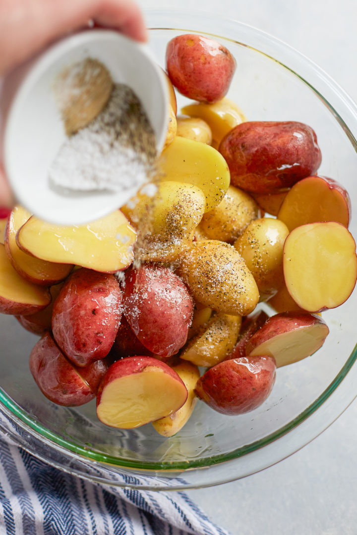 woman pouring seasonings over a bowl of potatoes