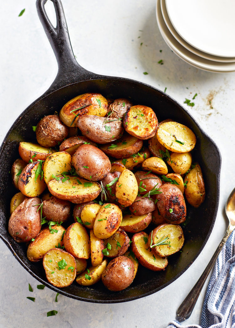 a cast iron pan with traeger roasted potatoes next to a stack of white plates