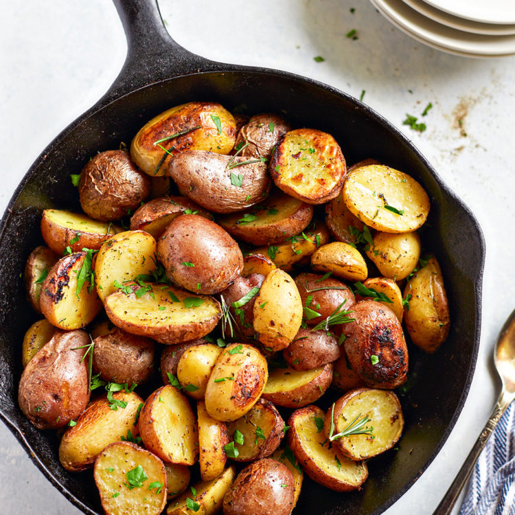 a cast iron pan with traeger roasted potatoes next to a stack of white plates