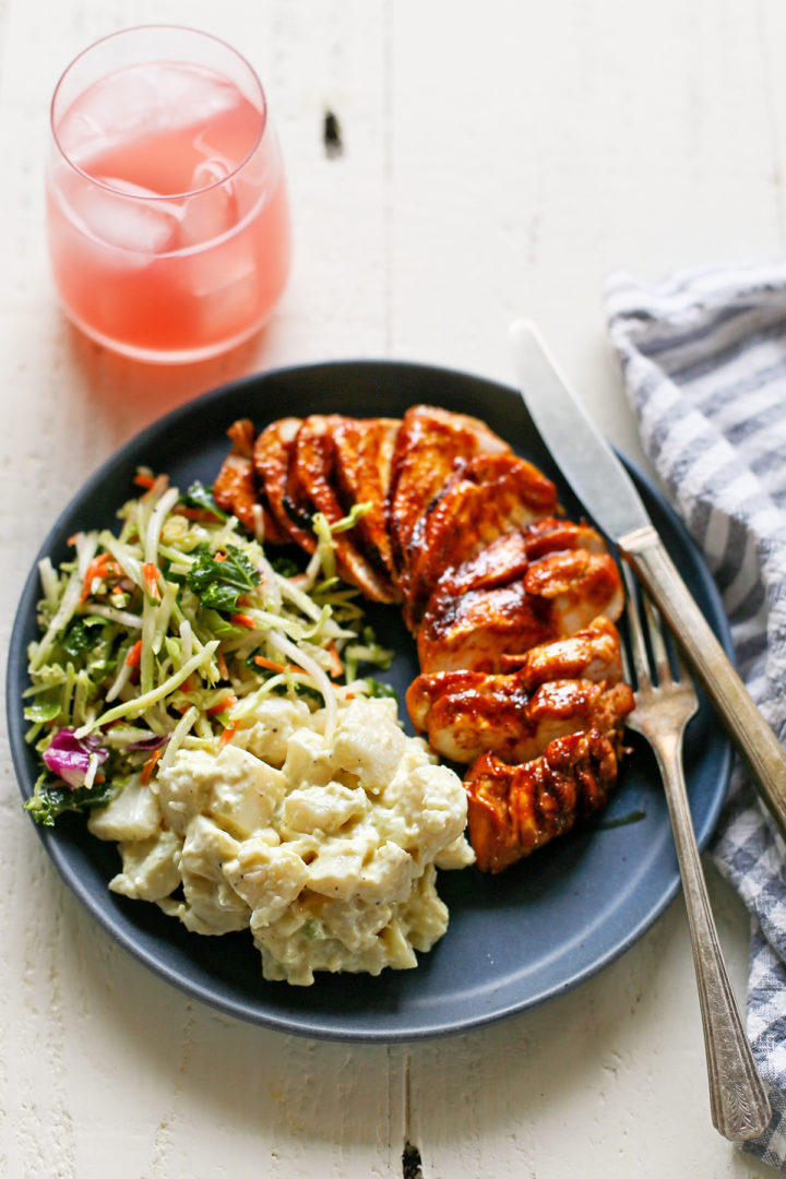 a white wooden table set with a dinner plate featuring grilled bbq chicken and side dishes