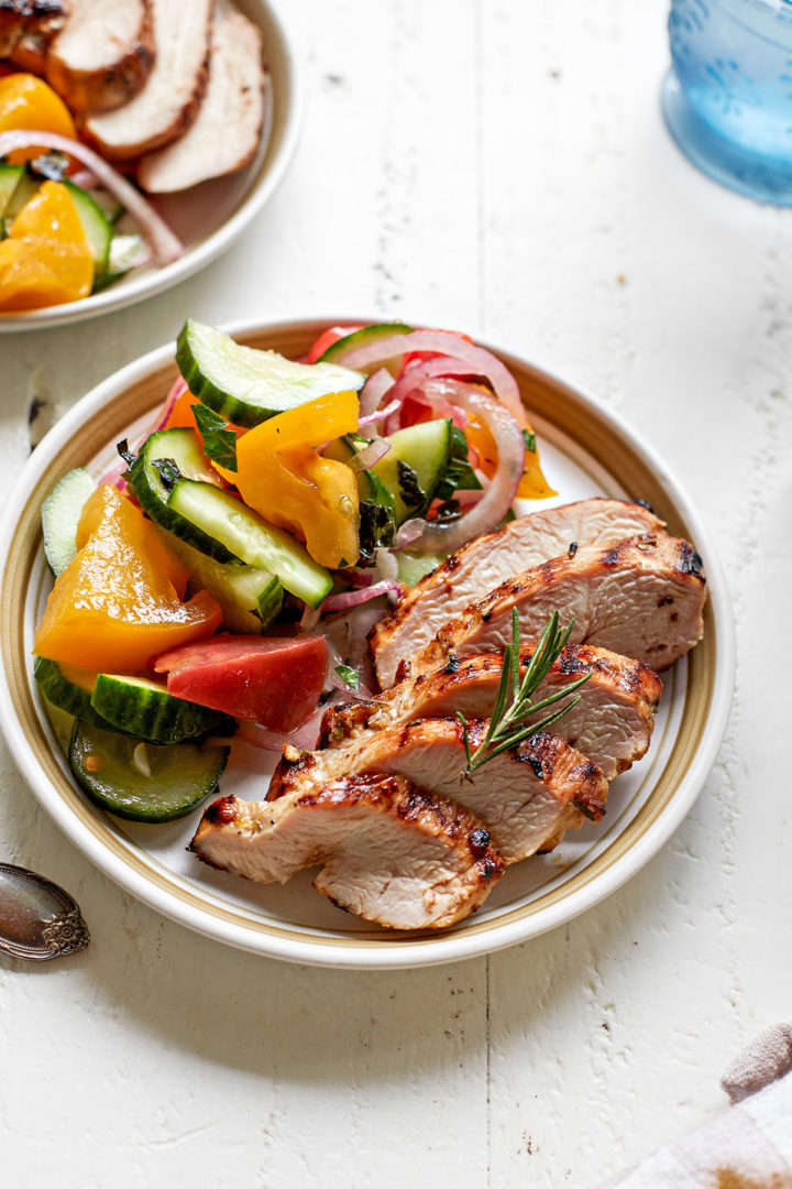 close up of sliced chicken with lemon, garlic, and rosemary on a plate