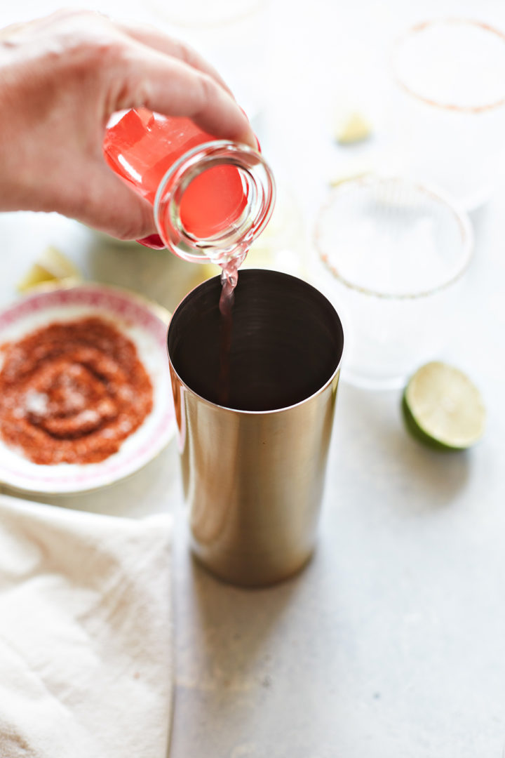 woman adding fresh watermelon juice to a cocktail shaker