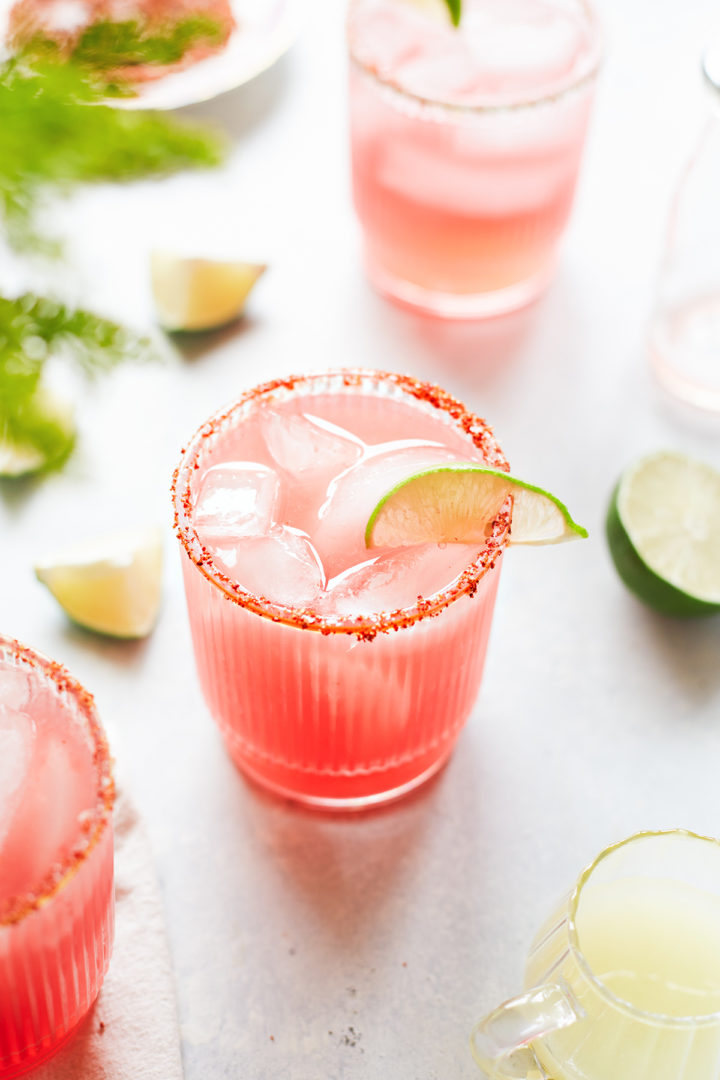 three glasses of watermelon margarita with a spicy salt rim and lime garnishes