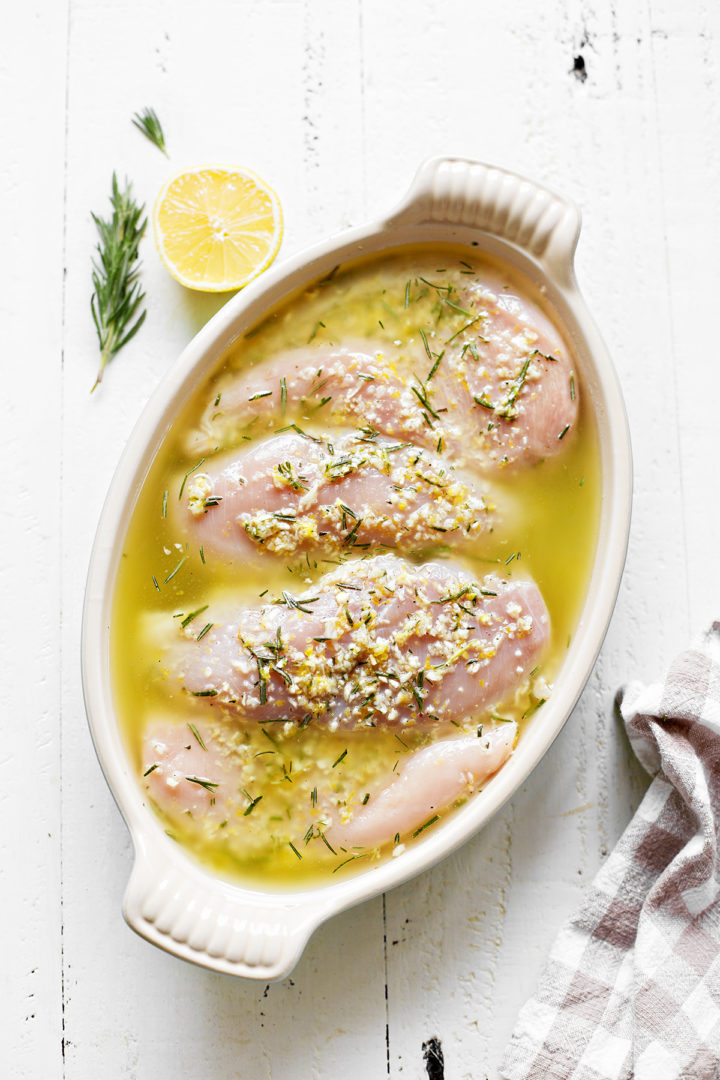 chicken marinating in a dish of lemon rosemary marinade  