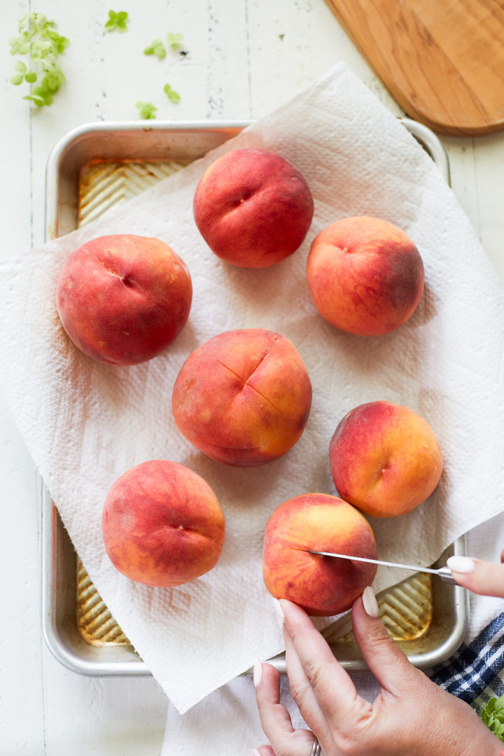 woman preparing peaches for blanching by scoring the bottoms with a knife